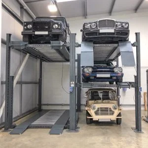 Two double car lifts next to each other. One is lifting a four wheel drive car, the other is holding two older cars with a third older car underneath.