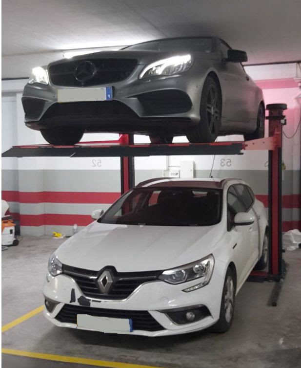 A black and red car lift, holding a grey car with a white car below.